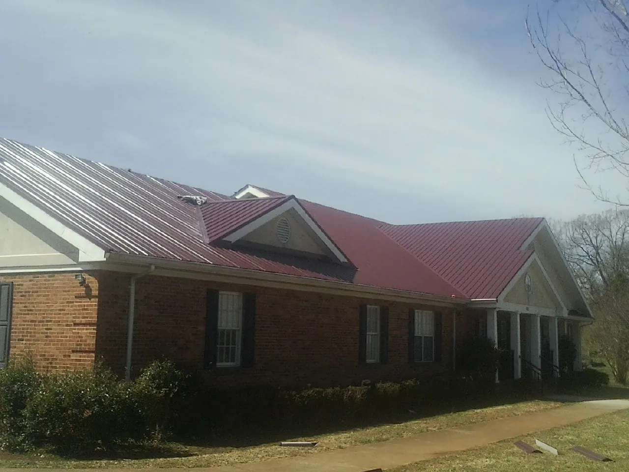 Red metal roof with gabled entries on a long brick building, from a Hail Damage Roof Repair job in Williamson